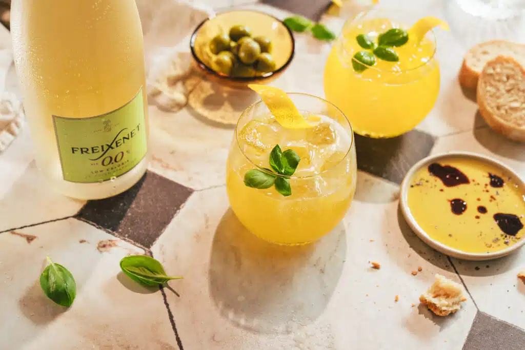 Gelbe Sommerdrinks mit Snacks und einer Flasche Freixenet