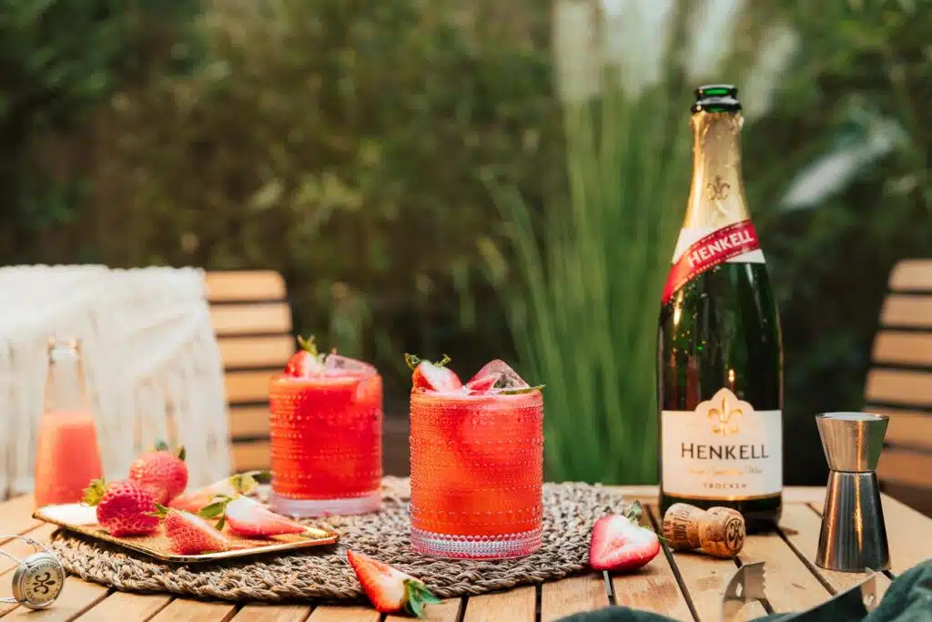 Sommerdrinks mit Erdbeeren neben einer Sektflasche im Garten