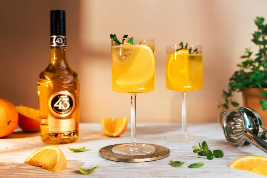Zwei Sommerdrinks mit Orange vor einer Likörflasche