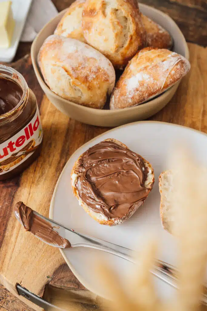 Frische Brötchen im Korb, eins mit Nutella bestrichen