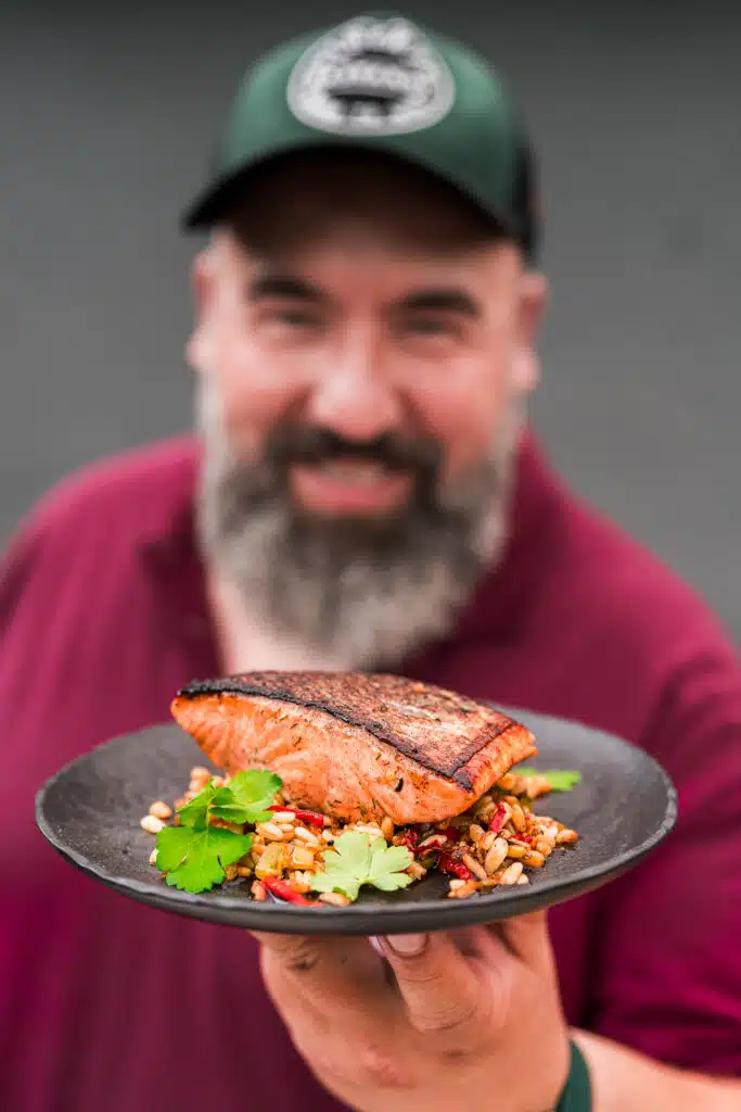 Brandface mit Basecap hält einen Teller mit gegrilltem Lachs